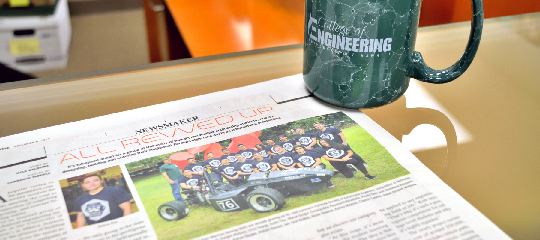 Photo Of CoE Mug On A Copy Of Article About UH SAE Team In MidWeek Newspaper.