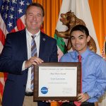 A man in a suit holding a NASA plaque with UH alumnus and awardee Evan Kawamura