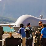 Researchers and military personnel chatting in front of a drone