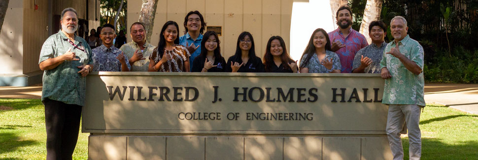 A Group Of People Posing For A Photo Around The Holmes Hall Sign